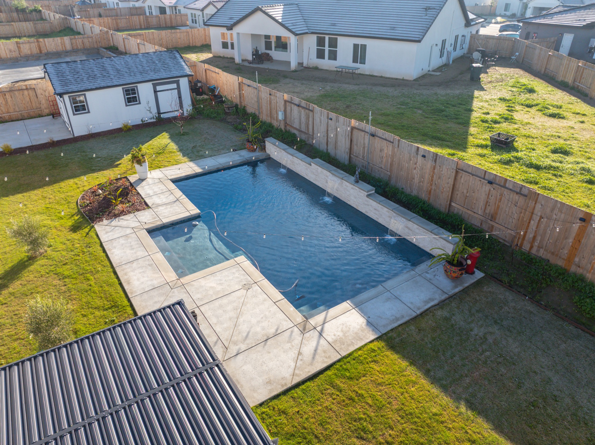 Aerial view of custom gunite pool with dark plaster finish and solar panels in Bakersfield